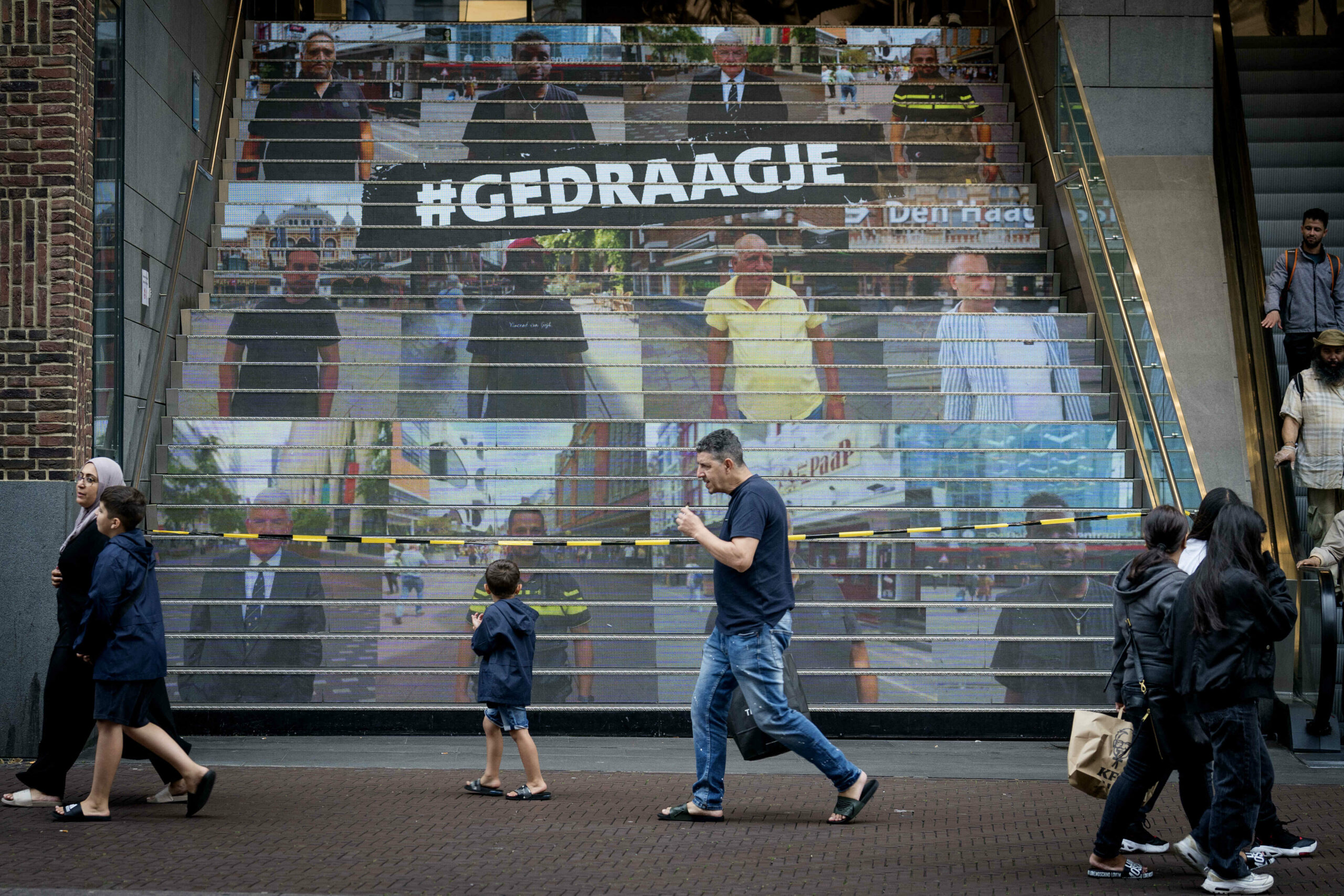 Spuimarkttrap met daarop de acht Haagse mannen in beeld, met in het midden campagneslogan #GEDRAAGJE